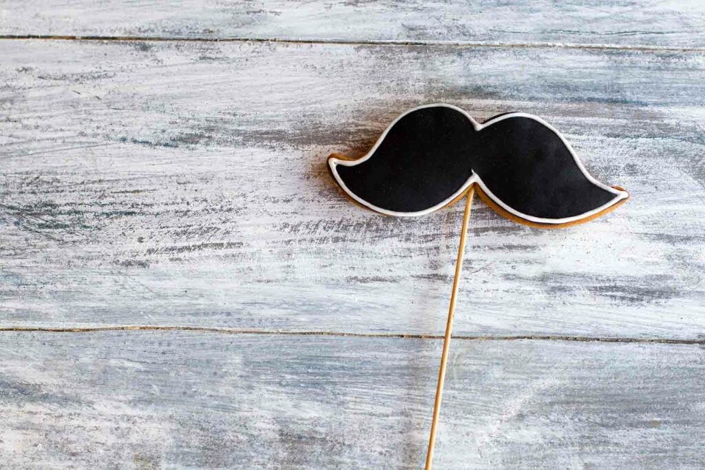 A movember mustache on a stick on a wooden table.