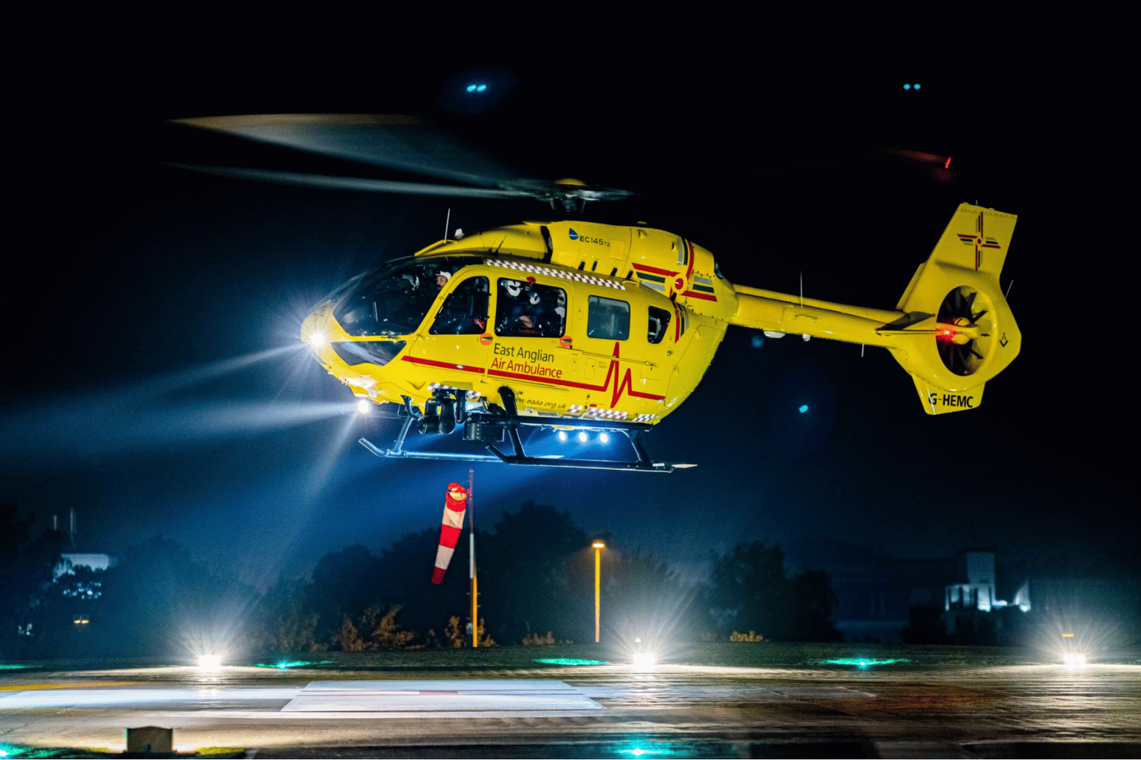 A yellow helicopter participating in the East Anglian Air Ambulance Raffle, flying at night.